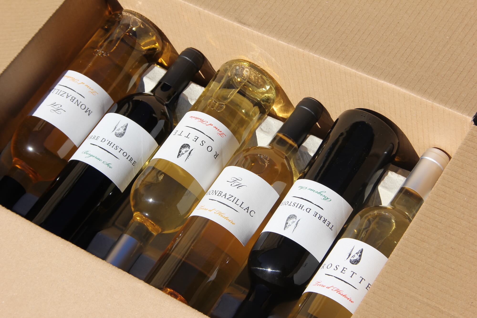 six bouteilles de vin blanc couchées en quinconces dans un carton deux bouteilles de verre foncé et quatre bouteilles de verre blanc