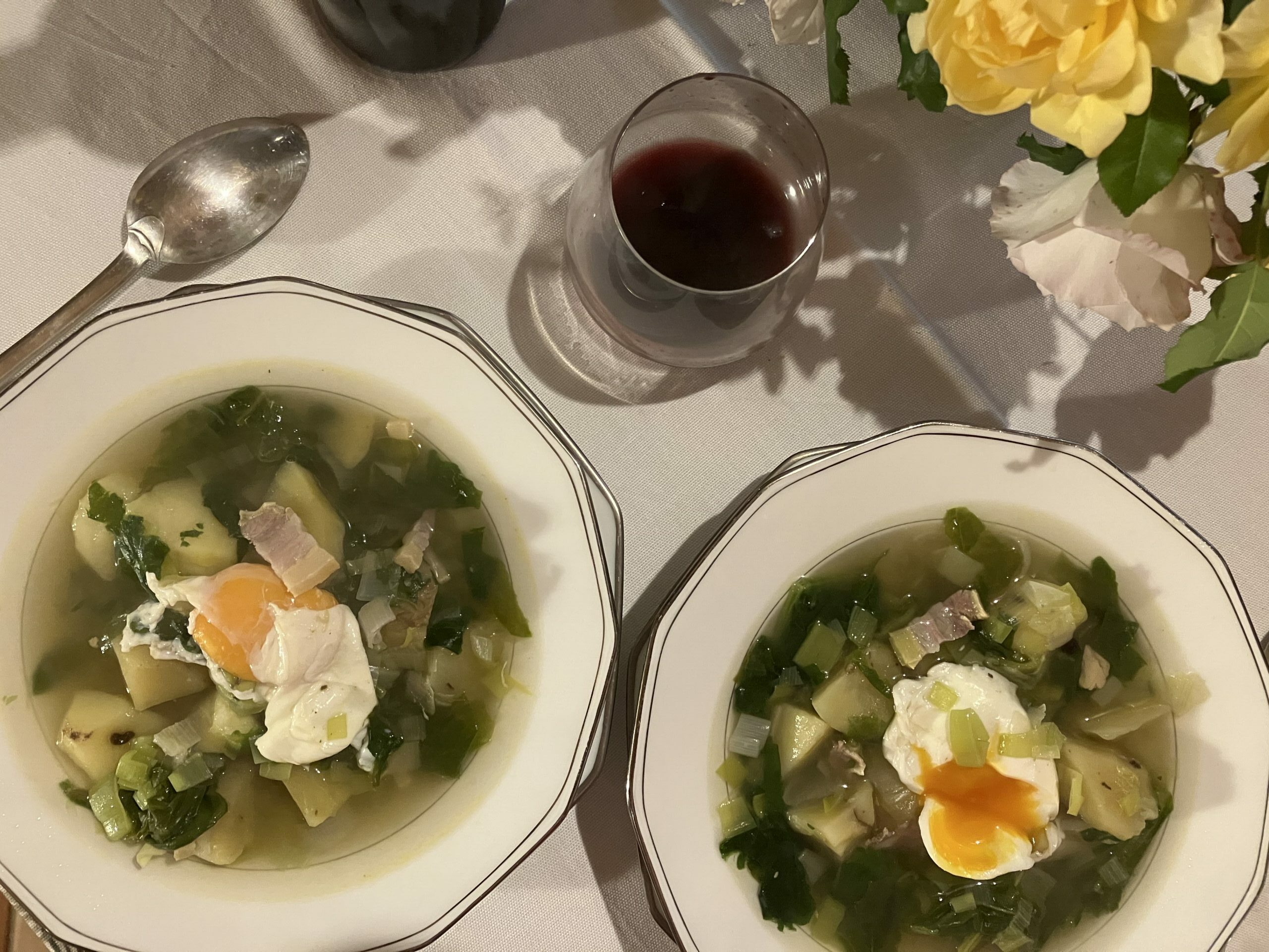 deux assiettes à soupe garnie d'une soupe aux légumes avec des oeufs pochés au dessus et un verre de vin à côté photo prise de haut