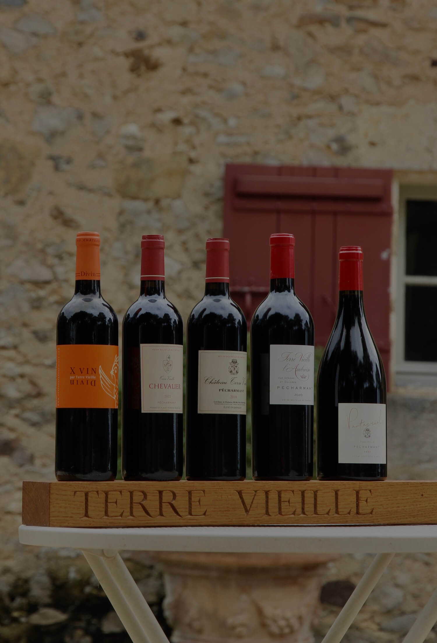 Bouteilles de vin posées sur un présentoir en bois "Terre Vieille", fond de mur de pierre, ambiance authentique et traditionnelle.