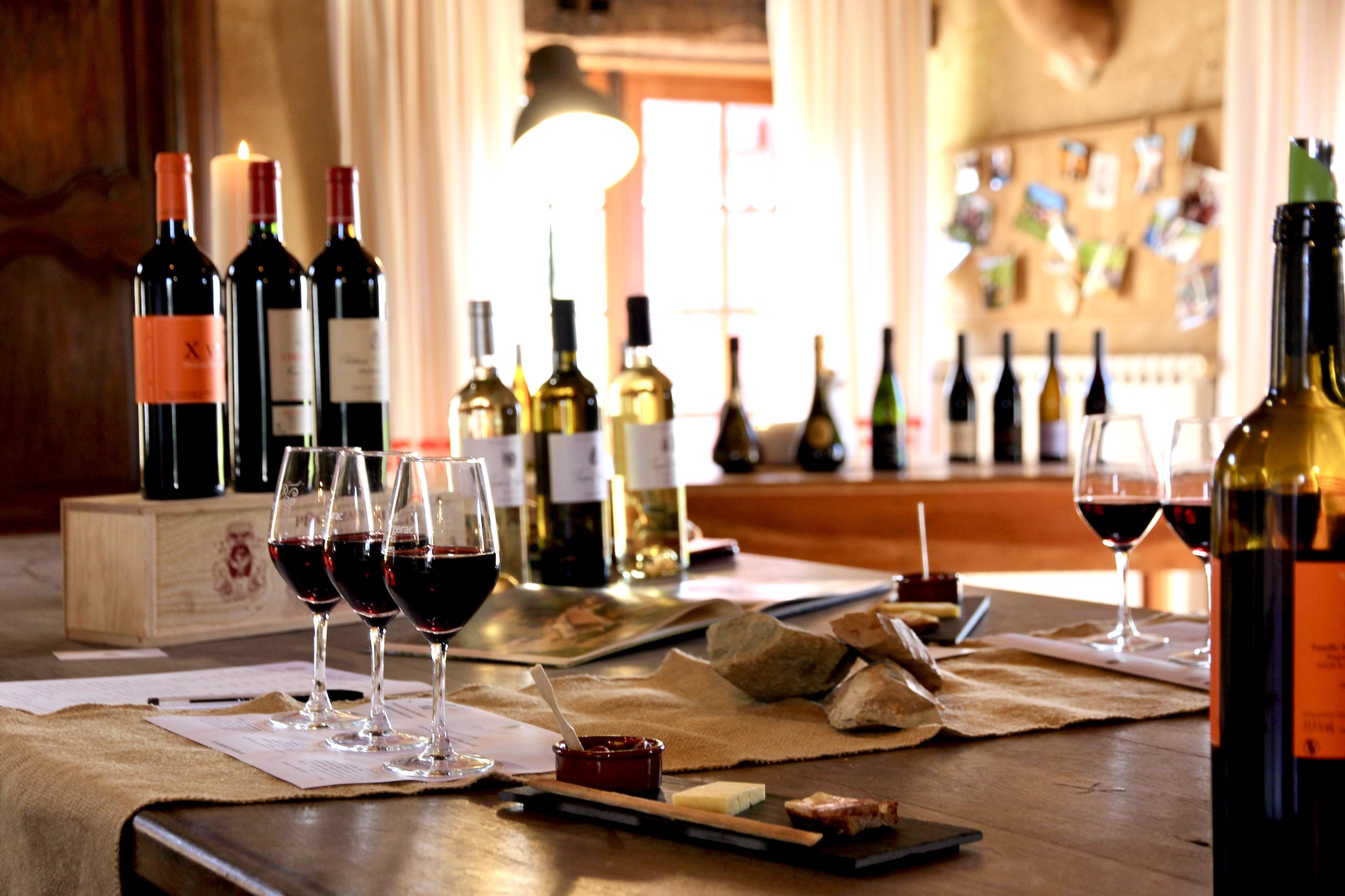 Trois verres de vin et des bouchées d'accord mets et vins sur une table en bois, avec une lumière tamisée illuminant les bouteilles et l'ambiance chaleureuse de Terre Vieille.